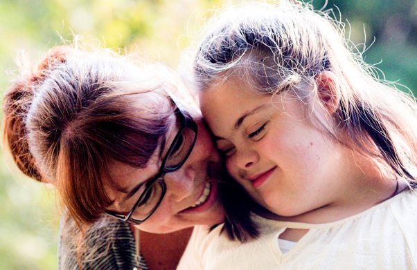 Photograph of a smiling mother hugging her daughter with Down syndrome Photograph of a smiling mother hugging her daughter with Down syndrome