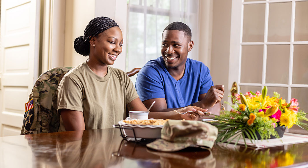 A young woman in military clothes eating pie with her husband at the kitchen table