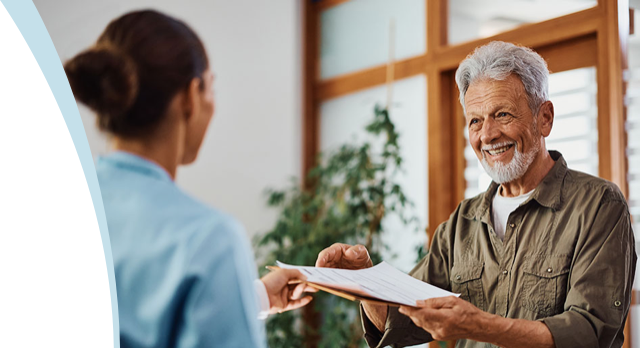 A nurse handing a clipboard across a desk to an older man